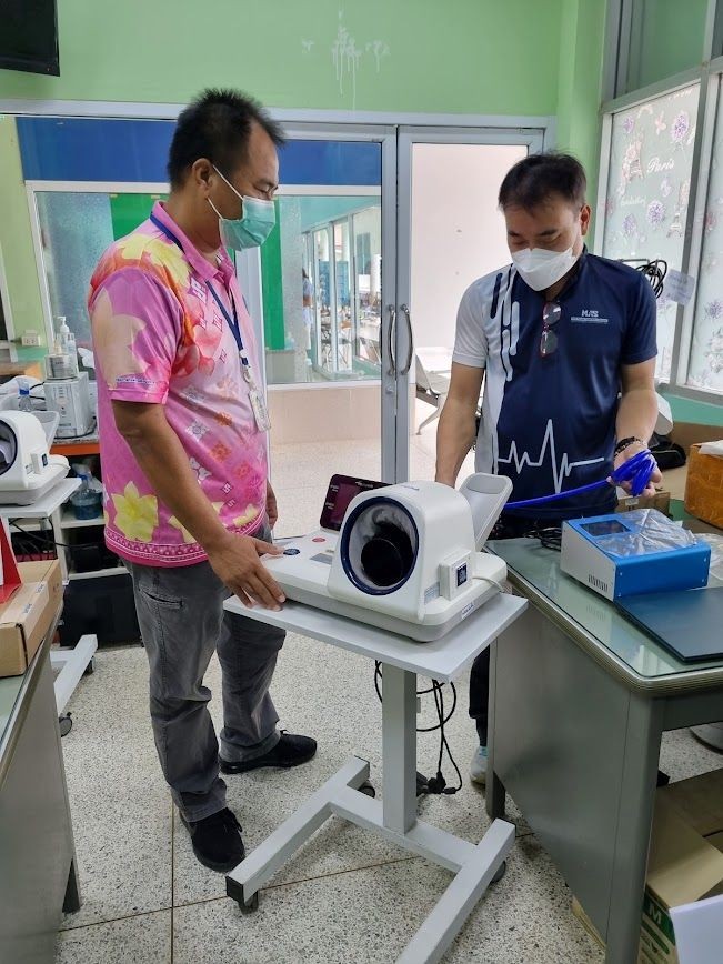 Two people in medical attire standing in a lab with a medical device on a wheeled table.