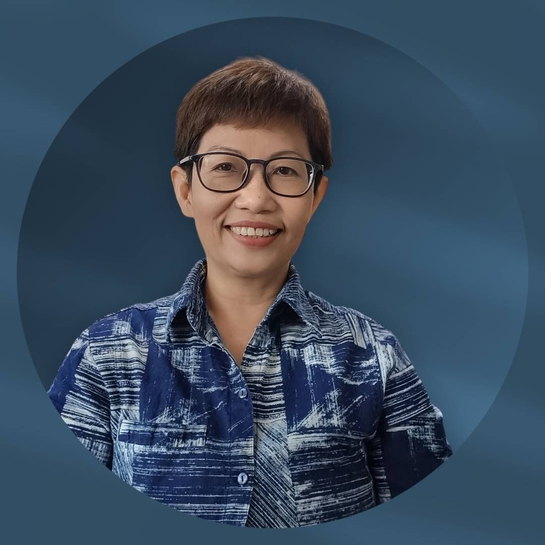 Person wearing a blue and white patterned button-up shirt, standing in front of a blue background.