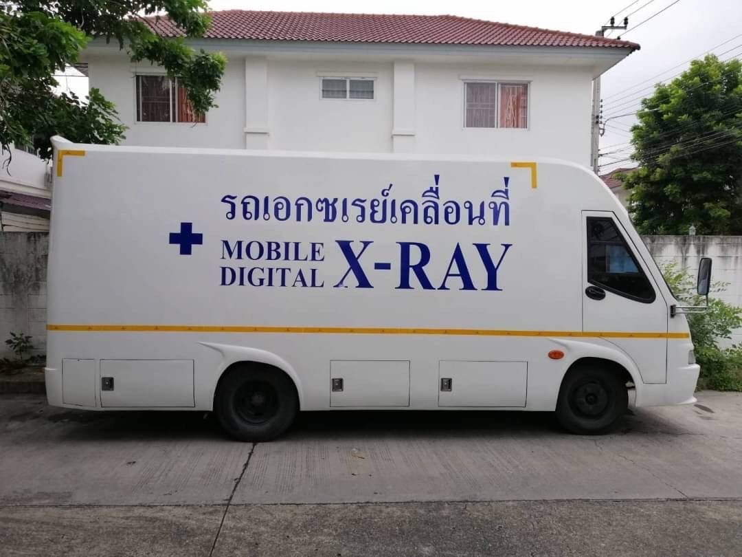 Side view of a mobile digital X-ray vehicle parked in front of a white building.